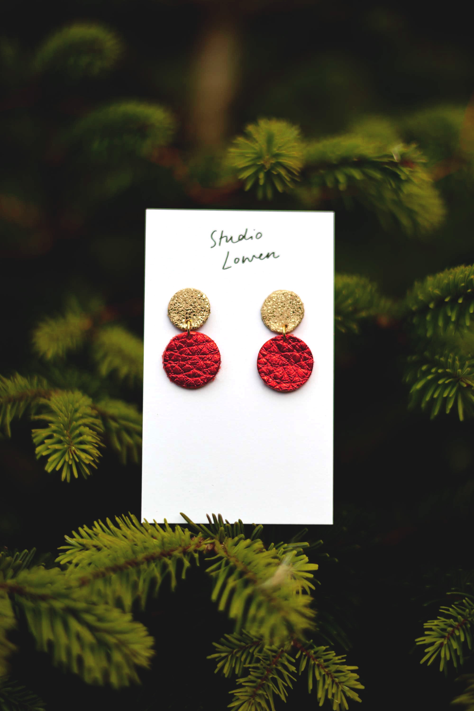 Red and gold earrings on a card with a green leafy Christmas tree background