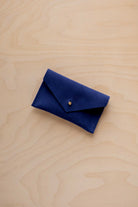 A small ultramarine blue coloured suede pouch with a flap closure and gold coloured fastening, on a light wood grain surface.