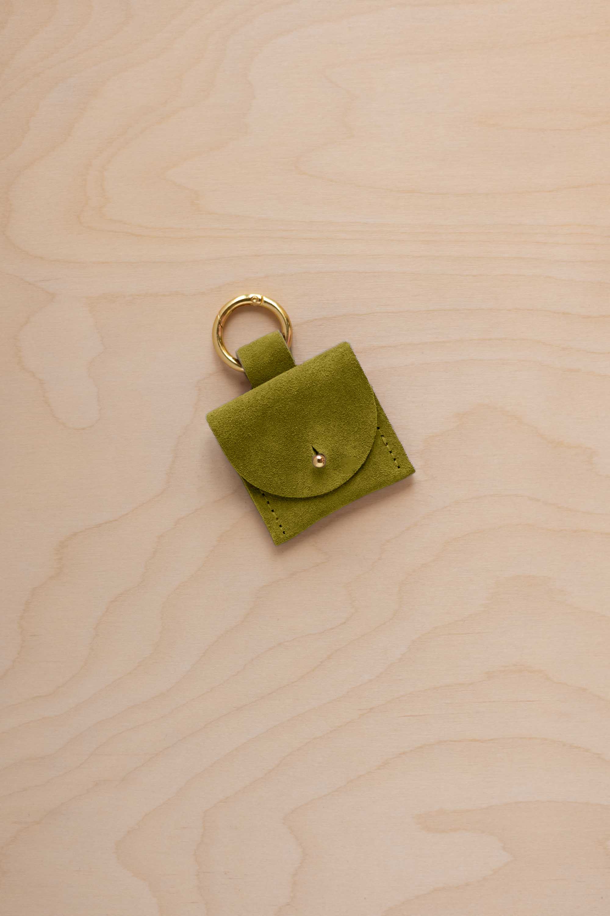 A small chartreuse lime green coloured suede pouch bag charm with a gold coloured clip ring fastening, displayed on a light wood grain background.