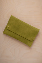 A chartreuse lime green coloured suede clutch with small gold coloured metal studs, displayed diagonally on a light wood grain surface.