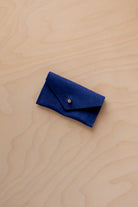 A small ultramarine blue coloured suede jewellery pouch with a gold coloured fastening, resting on a light wood grain surface.