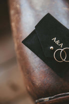 Small black suede jewellery pouch with gold foiled couples initials on the front with two gold wedding rings.