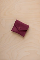 A small burgundy suede pouch with a gold button, placed on a light wood grain surface.