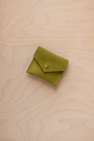 A small chartreuse green suede jewelry pouch with a gold button, resting on a light wood grain surface.
