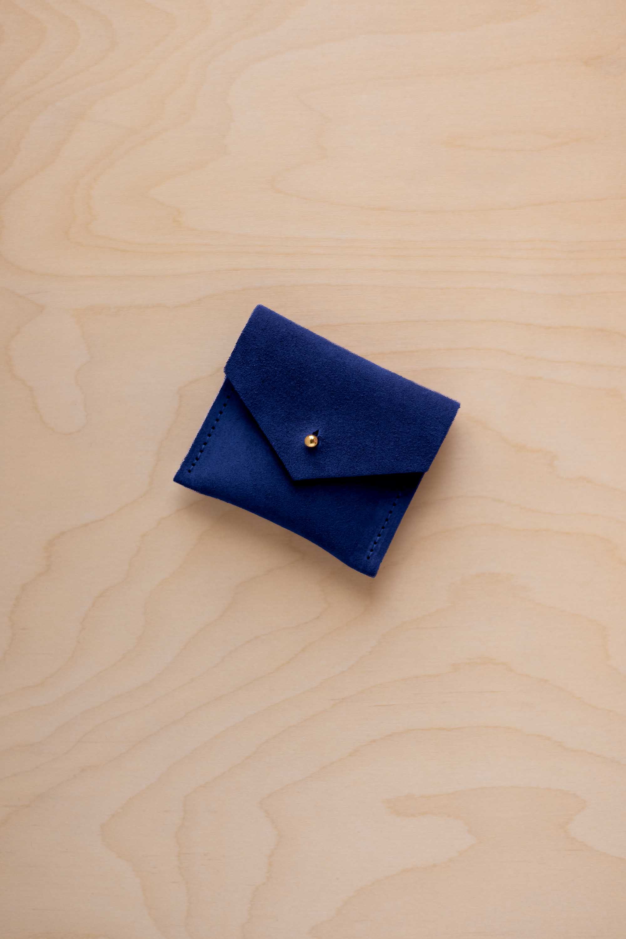 A small dark royal blue felt pouch with a flap closure and a gold button, placed on a light wood grain surface.