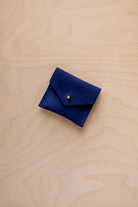 A small dark royal blue felt pouch with a flap closure and a gold button, placed on a light wood grain surface.