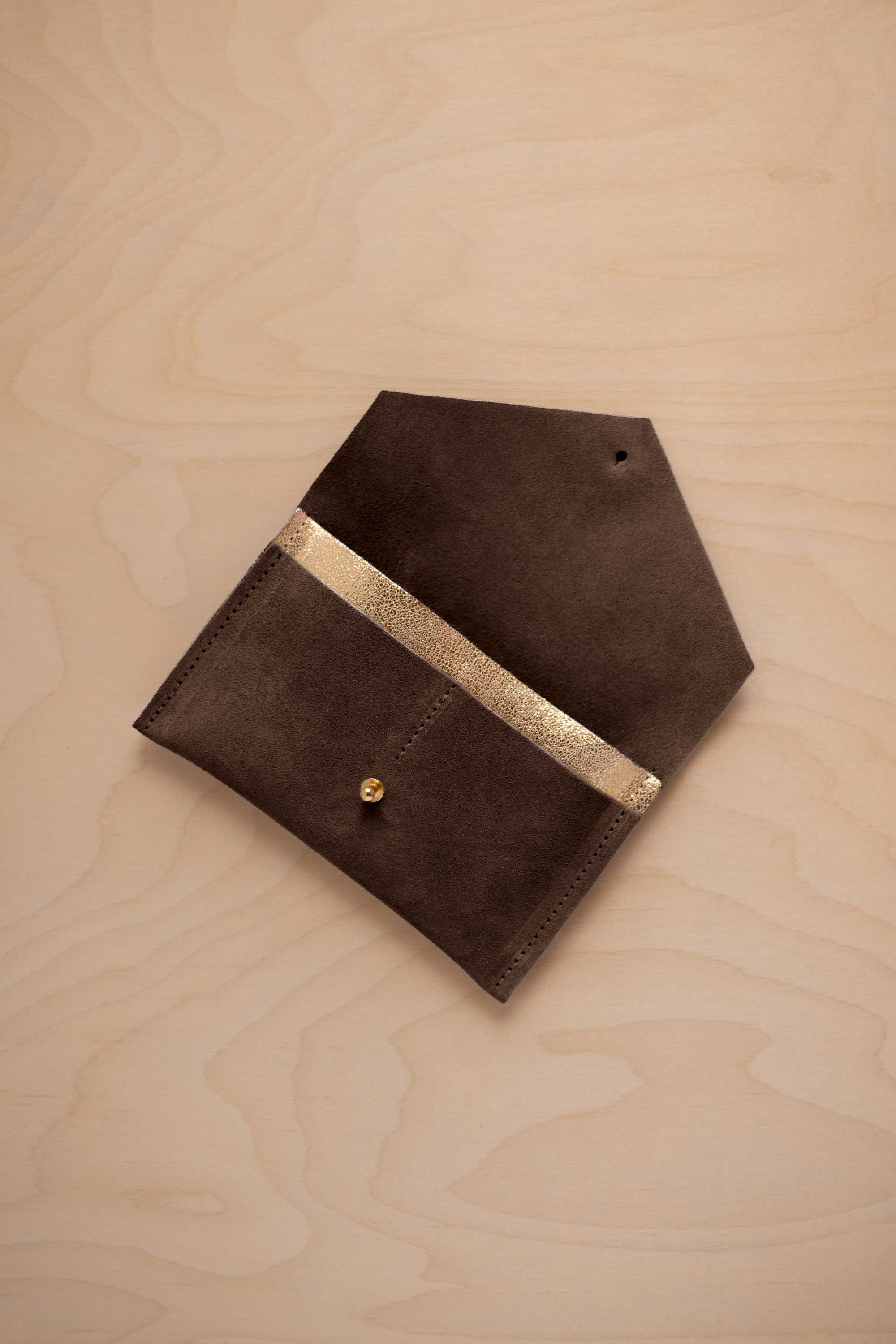 An espresso brown coloured suede pouch with a metallic gold contrast pocket and a small gold stud, displayed on a light wood grain background.