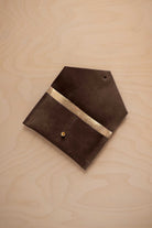 An espresso brown coloured suede pouch with a metallic gold contrast pocket and a small gold stud, displayed on a light wood grain background.