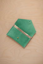 A seafoam turquoise green coloured suede pouch with a metallic gold contrast pocket and a small gold stud, displayed on a light wood grain background.