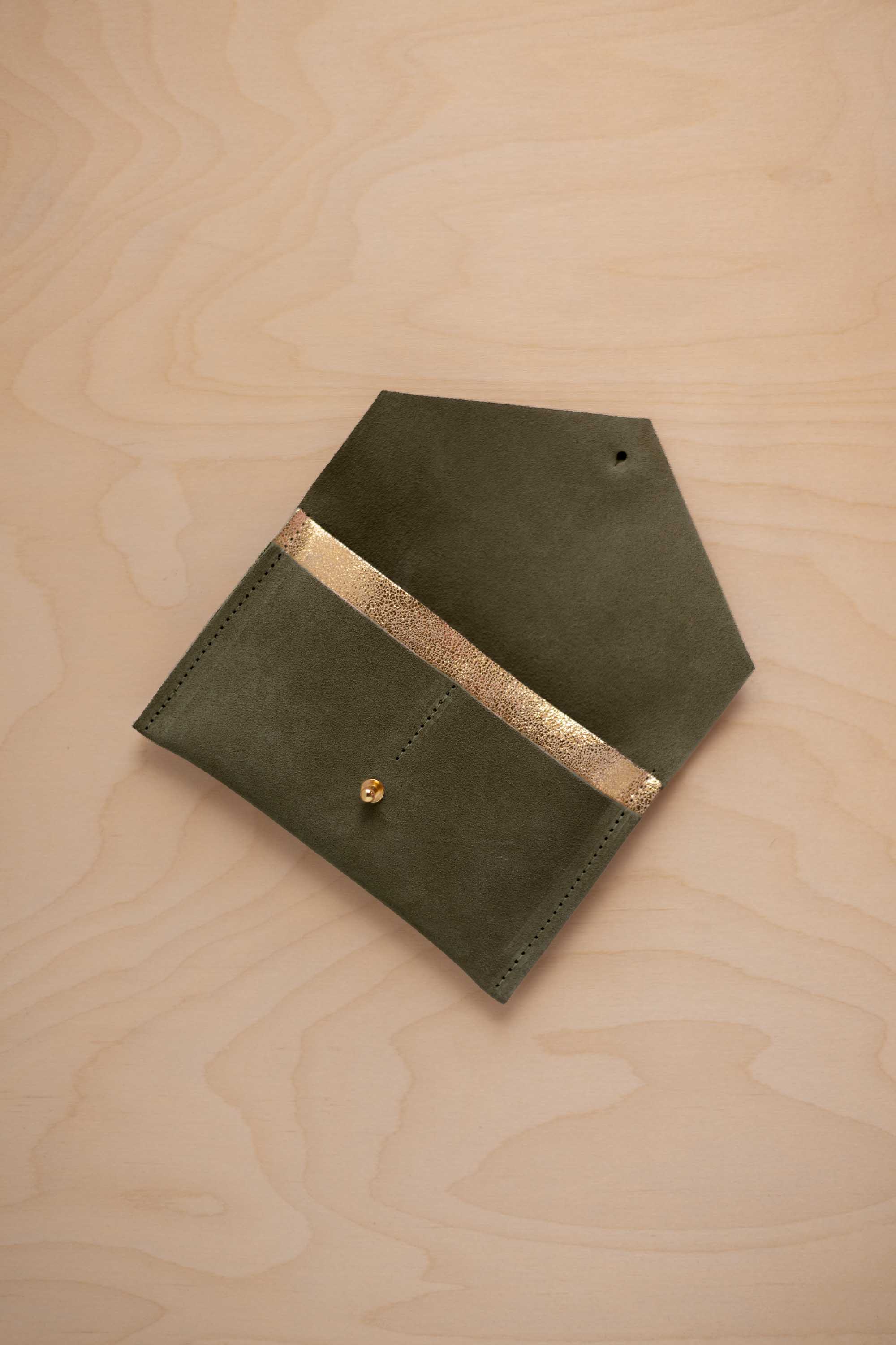 A soft olive green coloured suede pouch with a metallic gold contrast pocket and a small gold stud, displayed on a light wood grain background.