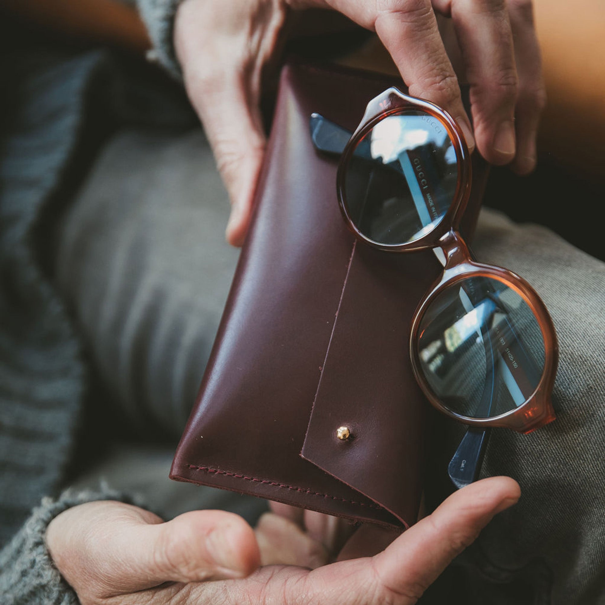 Brown leather glasses case with brown rimmed glasses being held in mans hands.