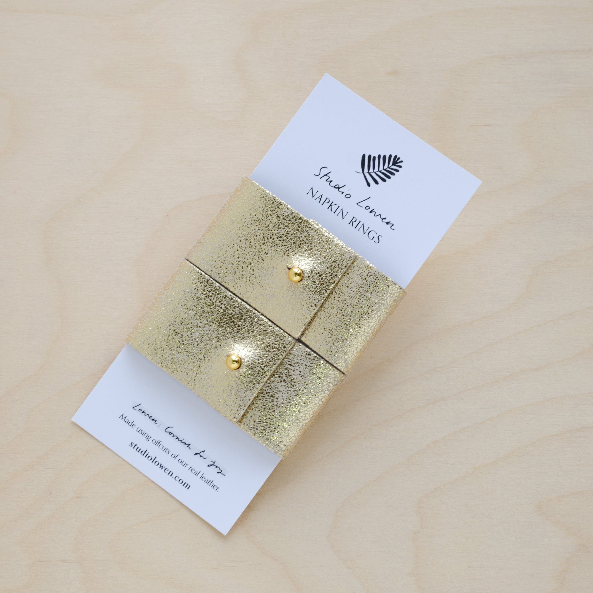 Pair of gold leather napkin rings in a metallic gold leather with a gold stud on white packaging.