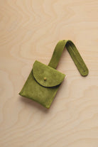 A small chartreuse lime green suede pouch with a flap closure and a matching strap, resting on a light wood grain surface.